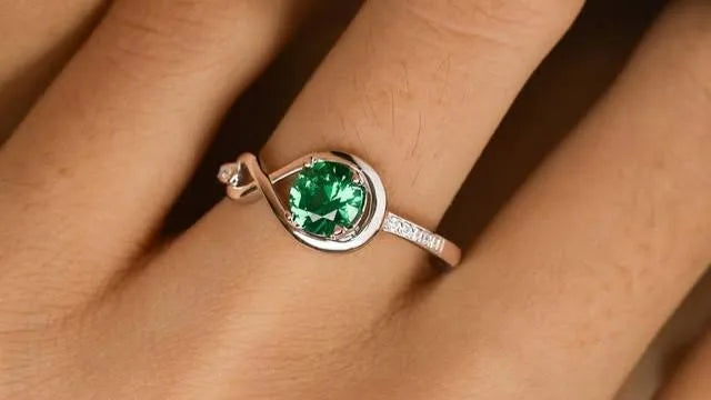 A ring with a large round green gemstone on a finger.