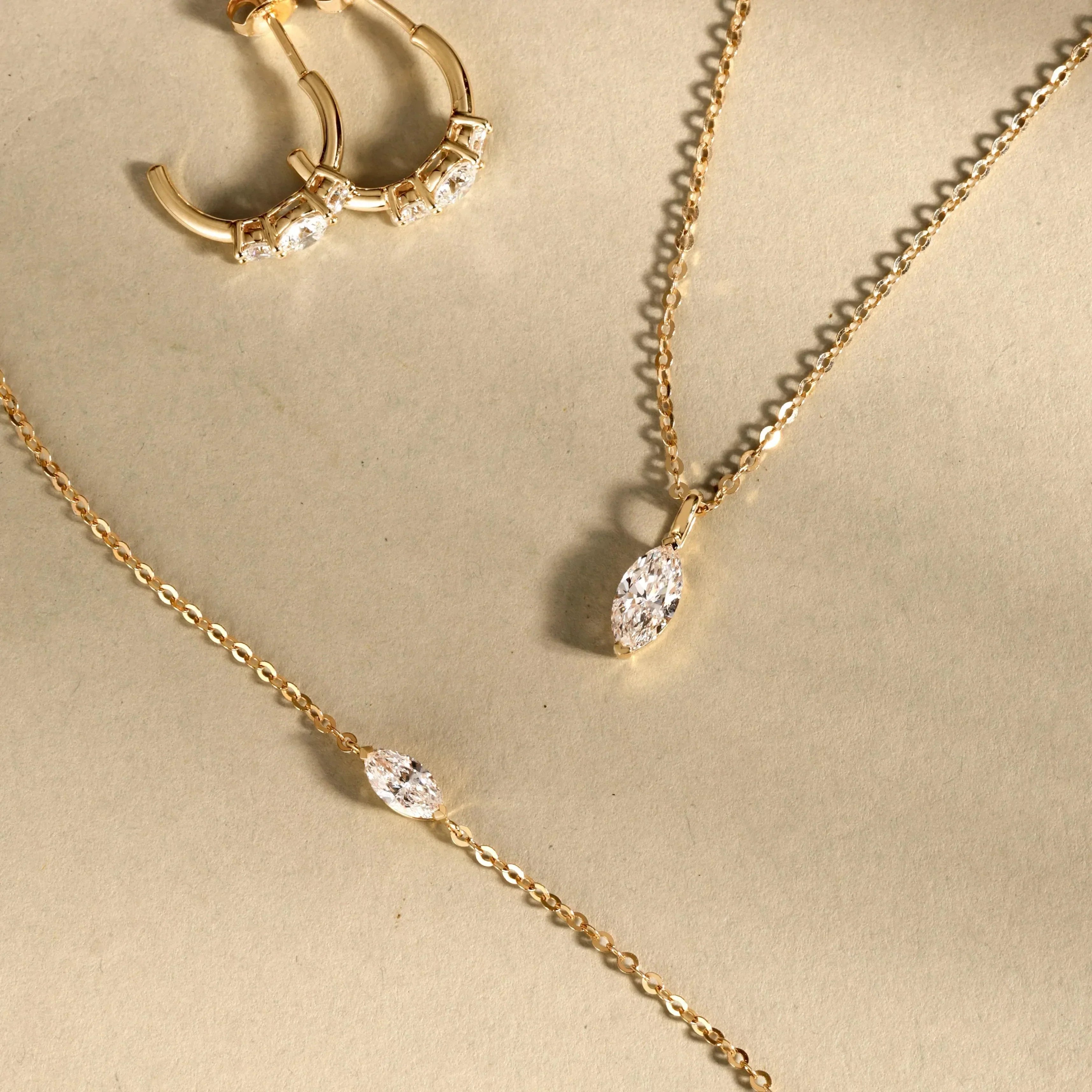Gold-tone jewelry set with clear marquise stones: hoops, pendant necklace, bracelet.