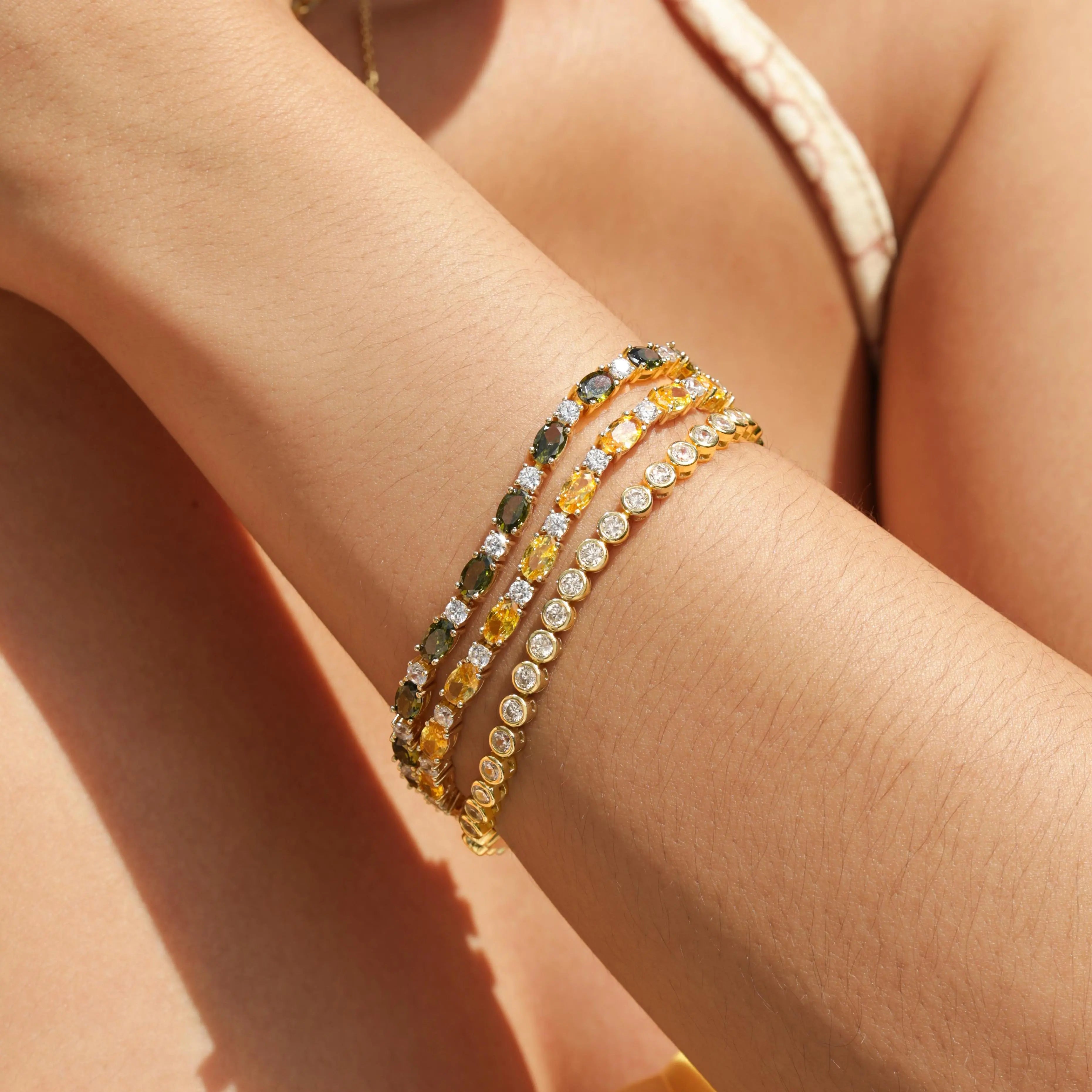 Stackable gold tennis bracelets with green, yellow gemstones and clear crystals on wrist